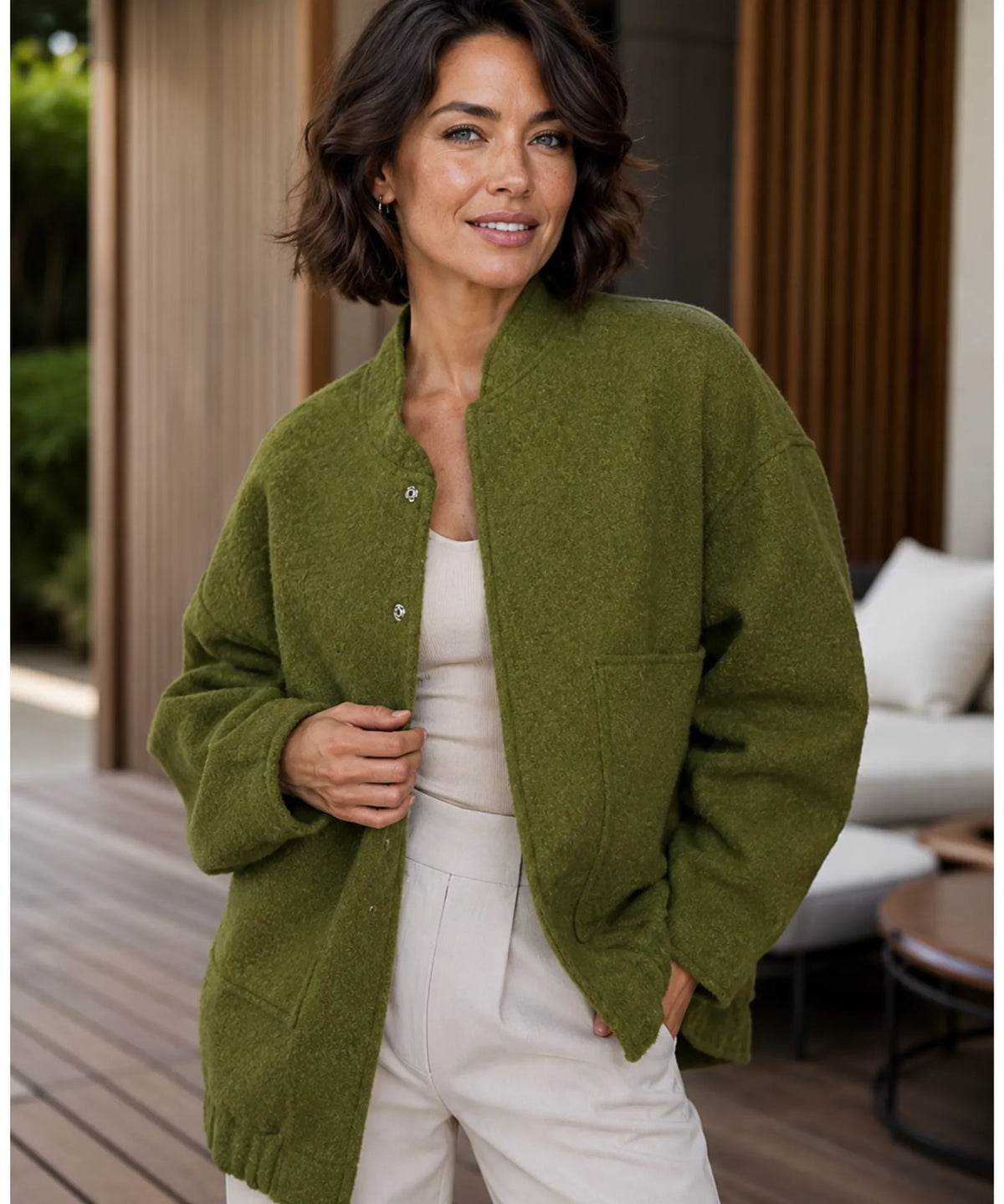 Woman layering oversized bouclé bomber jacket over a dress in camel