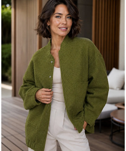 Woman layering oversized bouclé bomber jacket over a dress in camel